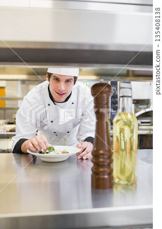 Male chef plating salad on white plate at commercial kitchen pass beside pepper mill Male chef plating salad on white plate at commercial kitchen pass beside pepper mill 135408138
