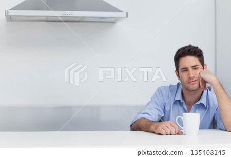 Man sitting at kitchen counter supporting head with hand while holding white mug, copy space Man sitting at kitchen counter supporting head with hand while holding white mug, copy space 135408145