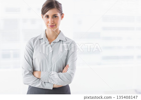 Woman in gray collared shirt standing with crossed arms in office with digital interface graphics Woman in gray collared shirt standing with crossed arms in office with digital interface graphics 135408147