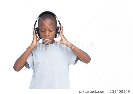 African American boy standing in studio against white backdrop holding headphones at ear level 135408149