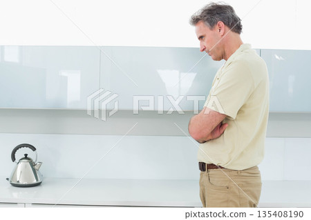 Middle-aged man standing at kitchen countertop gazing at kettle by glossy cabinets, copy space 135408190