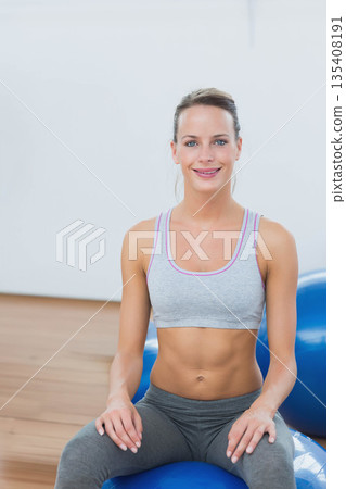 Fit woman strengthening core by balancing on blue exercise ball with second ball in fitness studio 135408191