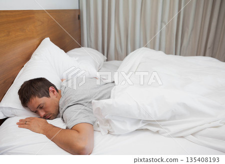 Man lying face down in bedroom on bed with wooden headboard, white duvet, copy space Man lying face down in bedroom on bed with wooden headboard, white duvet, copy space 135408193