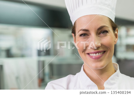 Female chef standing in commercial kitchen with counters wearing chef hat and jacket, copy space Female chef standing in commercial kitchen with counters wearing chef hat and jacket, copy space 135408194