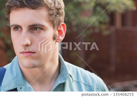 Male looking off right side in garden wearing light blue shirt, carrying backpack strap, copy space Male looking off right side in garden wearing light blue shirt, carrying backpack strap, copy space 135408255