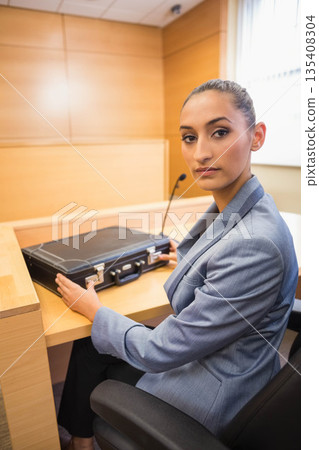 Female lawyer in suit placing briefcase on courtroom witness desk next to microphone, copy space Female lawyer in suit placing briefcase on courtroom witness desk next to microphone, copy space 135408304