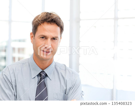 Mid-adult man standing with arms crossed at office by white shutters in dress shirt and tie Mid-adult man standing with arms crossed at office by white shutters in dress shirt and tie 135408323