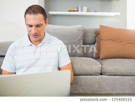 Mid adult male working on silver laptop while sitting on floor in living room, copy space Mid adult male working on silver laptop while sitting on floor in living room, copy space 135408333