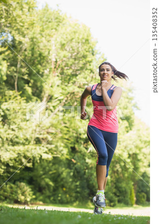 Woman running on grassy park trail wearing bright tank top dark leggings and running shoes Woman running on grassy park trail wearing bright tank top dark leggings and running shoes 135408352