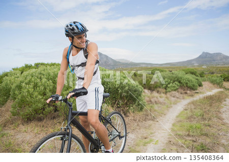 White adult male cyclist pausing on mountain bike on dirt trail wearing helmet and hydration pack White adult male cyclist pausing on mountain bike on dirt trail wearing helmet and hydration pack 135408364