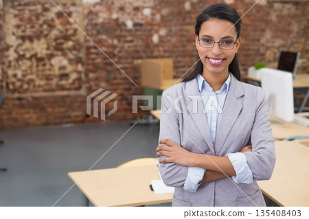 African American woman standing in loft office wearing grey blazer at desk with plant, copy space 135408403