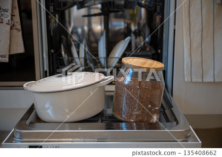Cozy kitchen still life with white cooking pot and glass jar of buckwheat on dishwasher door Cozy kitchen still life with white cooking pot and glass jar of buckwheat on dishwasher door 135408662