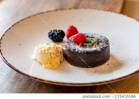 Chocolate fondant (cupcake) with raspberries, ice creme and powdered sugar placed on plate Chocolate fondant (cupcake) with raspberries, ice creme and powdered sugar placed on plate 135410166