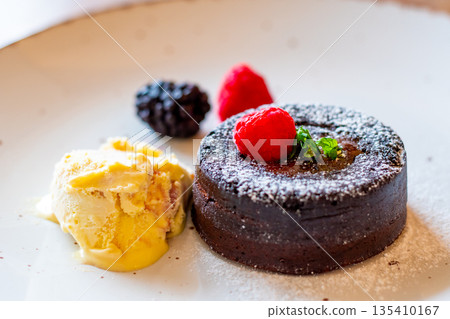Chocolate fondant (cupcake) with raspberries, ice creme and powdered sugar placed on plate 135410167