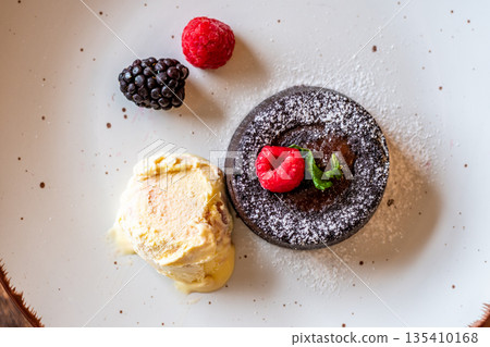 Chocolate fondant (cupcake) with raspberries, ice creme and powdered sugar placed on plate Chocolate fondant (cupcake) with raspberries, ice creme and powdered sugar placed on plate 135410168