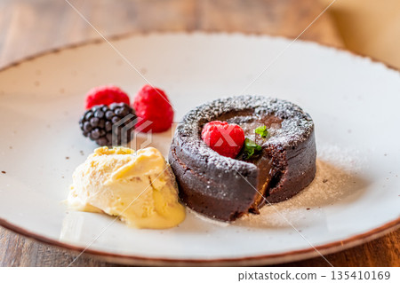 Chocolate fondant (cupcake) with raspberries, ice creme and powdered sugar placed on plate Chocolate fondant (cupcake) with raspberries, ice creme and powdered sugar placed on plate 135410169