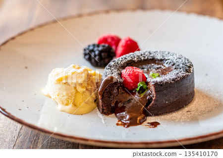 Chocolate fondant (cupcake) with raspberries, ice creme and powdered sugar placed on plate Chocolate fondant (cupcake) with raspberries, ice creme and powdered sugar placed on plate 135410170