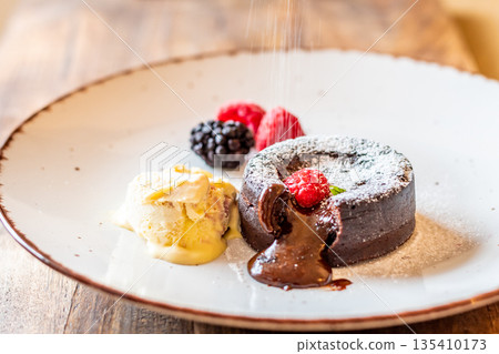Chocolate fondant (cupcake) with raspberries, ice creme and powdered sugar placed on plate 135410173