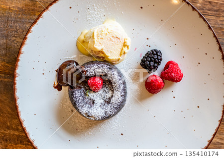 Chocolate fondant (cupcake) with raspberries, ice creme and powdered sugar placed on plate Chocolate fondant (cupcake) with raspberries, ice creme and powdered sugar placed on plate 135410174