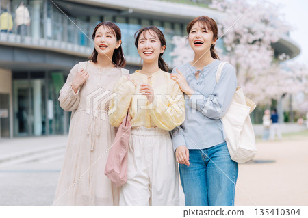 三位女大學生漫步在櫻花盛開的校園裡。 135410304