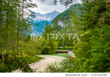 Famous green lake Schiederweiher near village Hinterstoder. Small weir and dam on lake with flowing water. Big Austrian mountains in background. Soft and magical colors in pure nature. Famous green lake Schiederweiher near village Hinterstoder. Small weir and dam on lake with flowing water. Big Austrian mountains in background. Soft and magical colors in pure nature. 135410365