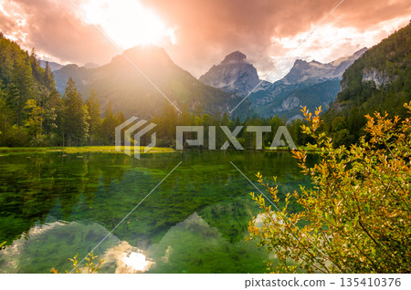 Famous green lake Schiederweiher near village Hinterstoder. Small weir and dam on lake with flowing water. Big Austrian mountains in background. Soft and magical colors in pure nature. 135410376