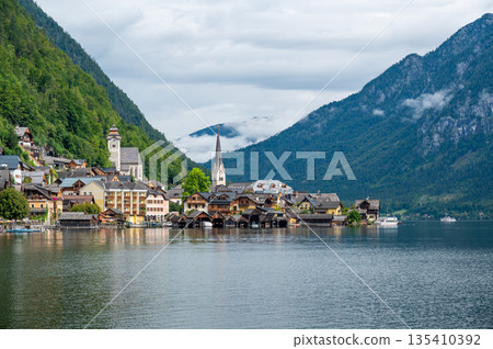 Hallstatt Village and Hallstatter See lake in Austria. Scenery with famous old church near the lake. Clouds and mist over the mountains in background. Famous tourist destination. 135410392