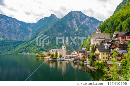 Famous view of Hallstatt city and church near the lake. Mountains in the background. Summer rainy day, soft colors, cloudy weather. Famous view of Hallstatt city and church near the lake. Mountains in the background. Summer rainy day, soft colors, cloudy weather. 135410396