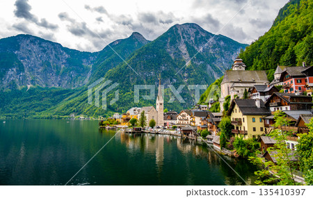 Famous view of Hallstatt city and church near the lake. Mountains in the background. Summer rainy day, soft colors, cloudy weather. Famous view of Hallstatt city and church near the lake. Mountains in the background. Summer rainy day, soft colors, cloudy weather. 135410397