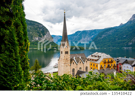 Famous Hallstatt city panorama with typical church near the Hallstatter see. Dramatic clouds on the sky. Famous tourist destination in Austria. 135410422