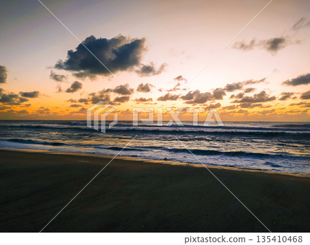 A breathtaking coastal landscape capturing a vibrant sunrise over the ocean. Golden waves and dramatic clouds create a peaceful scene, perfect for travel, wellness, or meditation themes. A breathtaking coastal landscape capturing a vibrant sunrise over the ocean. Golden waves and dramatic clouds create a peaceful scene, perfect for travel, wellness, or meditation themes. 135410468