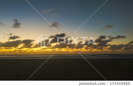 Capture the essence of peace with this stunning beach sunrise. The dramatic sky and golden light over the dark ocean create a perfect backdrop for travel, wellness, and creative projects. 135410489