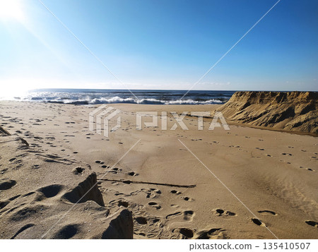 Experience coastal serenity with this sunlit beach vista. Footprints on golden sand suggest a journey toward rolling waves under a clear blue sky. Ideal for travel and nature projects. Experience coastal serenity with this sunlit beach vista. Footprints on golden sand suggest a journey toward rolling waves under a clear blue sky. Ideal for travel and nature projects. 135410507