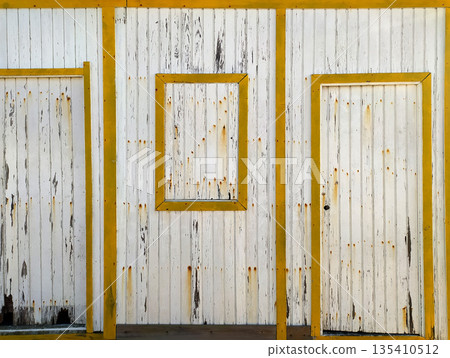 Rustic weathered wooden facade with peeling white paint and bold yellow frames. This textured vintage background evokes nostalgia and coastal charm, ideal for creative design projects. Rustic weathered wooden facade with peeling white paint and bold yellow frames. This textured vintage background evokes nostalgia and coastal charm, ideal for creative design projects. 135410512