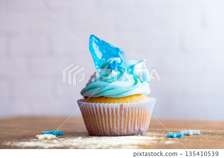 Homemade cupcake of blue color placed on wooden desk. Winter and christmas theme, snowflakes on cream with blue ice. Fresh and home baked sweet. Homemade cupcake of blue color placed on wooden desk. Winter and christmas theme, snowflakes on cream with blue ice. Fresh and home baked sweet. 135410539