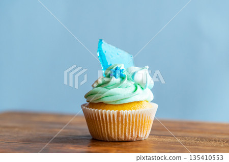 Homemade cupcake of blue color placed on wooden desk. Winter and christmas theme, snowflakes on cream with blue ice. Fresh and home baked sweet. Homemade cupcake of blue color placed on wooden desk. Winter and christmas theme, snowflakes on cream with blue ice. Fresh and home baked sweet. 135410553