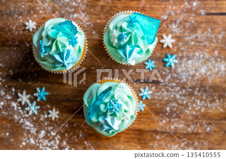 Homemade cupcake of blue color placed on wooden desk. Winter and christmas theme, snowflakes on cream with blue ice. Fresh and home baked sweet. Homemade cupcake of blue color placed on wooden desk. Winter and christmas theme, snowflakes on cream with blue ice. Fresh and home baked sweet. 135410555