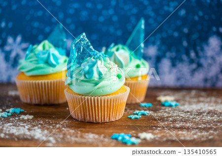 Homemade cupcake of blue color placed on wooden desk. Winter and christmas theme, snowflakes on cream with blue ice. Fresh and home baked sweet. Homemade cupcake of blue color placed on wooden desk. Winter and christmas theme, snowflakes on cream with blue ice. Fresh and home baked sweet. 135410565
