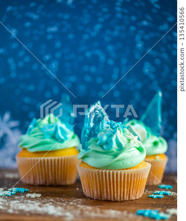 Homemade cupcake of blue color placed on wooden desk. Winter and christmas theme, snowflakes on cream with blue ice. Fresh and home baked sweet. Homemade cupcake of blue color placed on wooden desk. Winter and christmas theme, snowflakes on cream with blue ice. Fresh and home baked sweet. 135410566