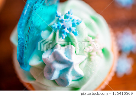 Homemade cupcake of blue color placed on wooden desk. Winter and christmas theme, snowflakes on cream with blue ice. Fresh and home baked sweet. Homemade cupcake of blue color placed on wooden desk. Winter and christmas theme, snowflakes on cream with blue ice. Fresh and home baked sweet. 135410569