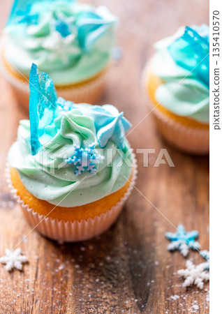 Homemade cupcake of blue color placed on wooden desk. Winter and christmas theme, snowflakes on cream with blue ice. Fresh and home baked sweet. 135410570