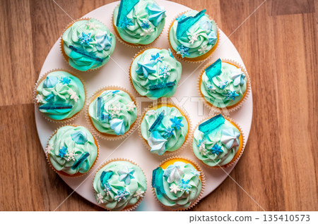 Homemade cupcake of blue color placed on wooden desk. Winter and christmas theme, snowflakes on cream with blue ice. Fresh and home baked sweet. 135410573