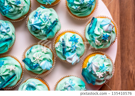 Homemade cupcake of blue color placed on wooden desk. Winter and christmas theme, snowflakes on cream with blue ice. Fresh and home baked sweet. Homemade cupcake of blue color placed on wooden desk. Winter and christmas theme, snowflakes on cream with blue ice. Fresh and home baked sweet. 135410576