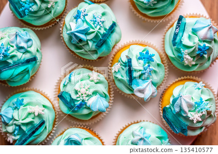 Homemade cupcake of blue color placed on wooden desk. Winter and christmas theme, snowflakes on cream with blue ice. Fresh and home baked sweet. Homemade cupcake of blue color placed on wooden desk. Winter and christmas theme, snowflakes on cream with blue ice. Fresh and home baked sweet. 135410577