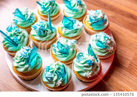 Homemade cupcake of blue color placed on wooden desk. Winter and christmas theme, snowflakes on cream with blue ice. Fresh and home baked sweet. 135410578