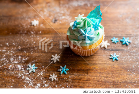 Homemade cupcake of blue color placed on wooden desk. Winter and christmas theme, snowflakes on cream with blue ice. Fresh and home baked sweet. 135410581
