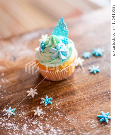 Homemade cupcake of blue color placed on wooden desk. Winter and christmas theme, snowflakes on cream with blue ice. Fresh and home baked sweet. Homemade cupcake of blue color placed on wooden desk. Winter and christmas theme, snowflakes on cream with blue ice. Fresh and home baked sweet. 135410582