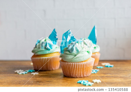 Homemade cupcake of blue color placed on wooden desk. Winter and christmas theme, snowflakes on cream with blue ice. Fresh and home baked sweet. 135410588
