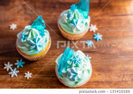 Homemade cupcake of blue color placed on wooden desk. Winter and christmas theme, snowflakes on cream with blue ice. Fresh and home baked sweet. Homemade cupcake of blue color placed on wooden desk. Winter and christmas theme, snowflakes on cream with blue ice. Fresh and home baked sweet. 135410589
