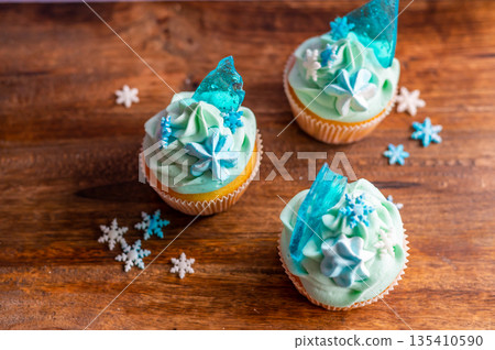 Homemade cupcake of blue color placed on wooden desk. Winter and christmas theme, snowflakes on cream with blue ice. Fresh and home baked sweet. 135410590